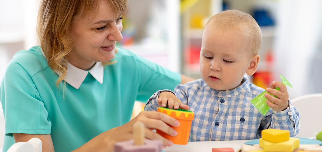 Woman and baby play with toys at table in nursery